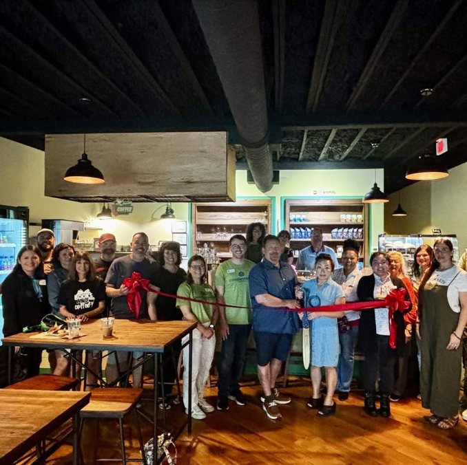 Inside Coffee House Haven during its ribbon cutting celebration — exposed ceiling, pendant lighting, and wood tables